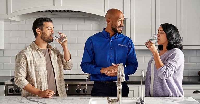 Culligan man standing between two people drinking glasses of water at kitchen sink